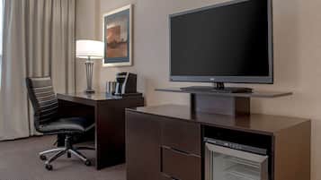 A hotel room with a desk, a television, a coffee maker, a chair, and a mini-fridge.