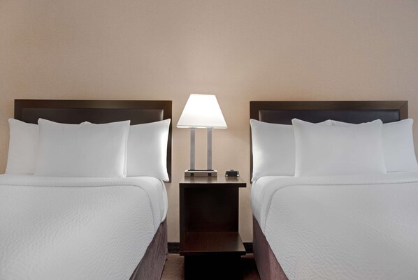 A hotel room with two beds, a nightstand with a lamp, and a small table. - Ramada Plaza by Wyndham Calgary Downtown (Calgary)