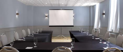 A conference room with a long table, chairs, a projector screen, and a large window.