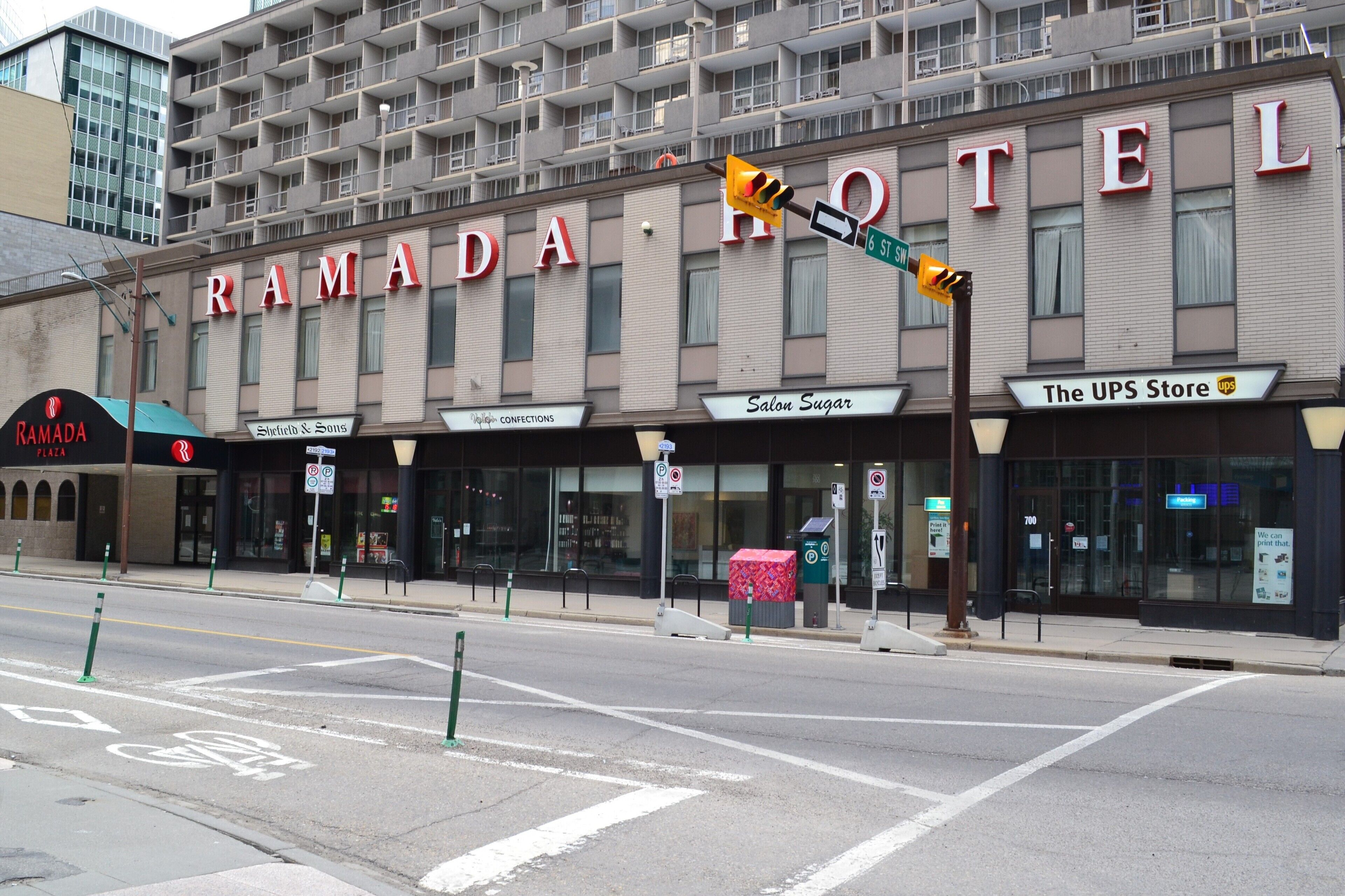 Un immeuble sur lequel on peut lire l’enseigne « RAMADA HOTEL » et qui abrite différents commerces, notamment « The UPS Store » et « Salon Sugar ».
