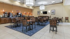 A hotel dining area with multiple tables and chairs, a coffee station, and a television mounted on the wall. - Best Western Plus Augusta Civic Center Inn (Augusta)