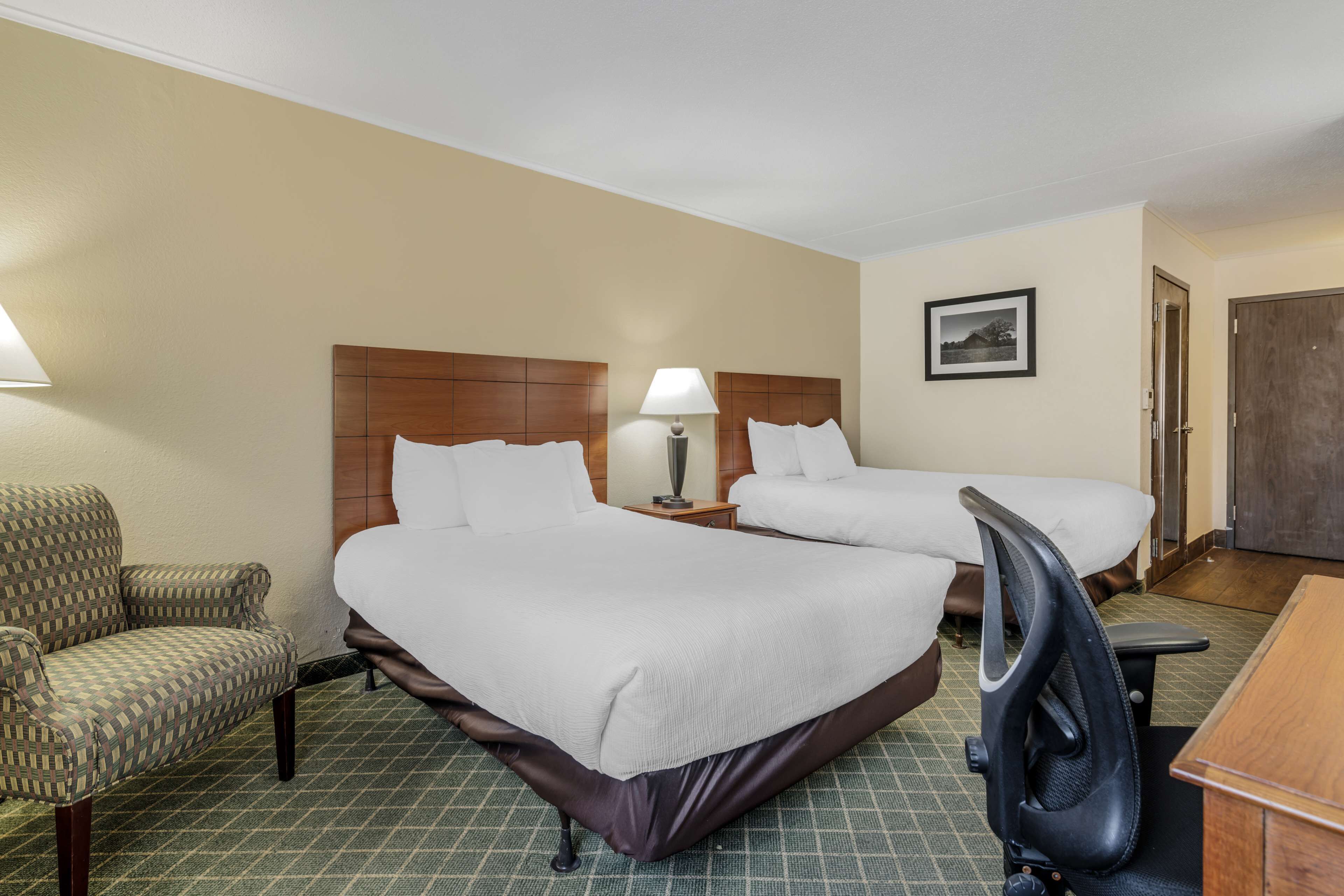 Una habitación de hotel con dos camas, una silla, un escritorio y una lámpara.