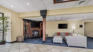 A hotel lobby with a large sectional sofa, a flat-screen TV mounted on the wall, a fireplace, and a potted plant. - Best Western Plus Augusta Civic Center Inn (Augusta)