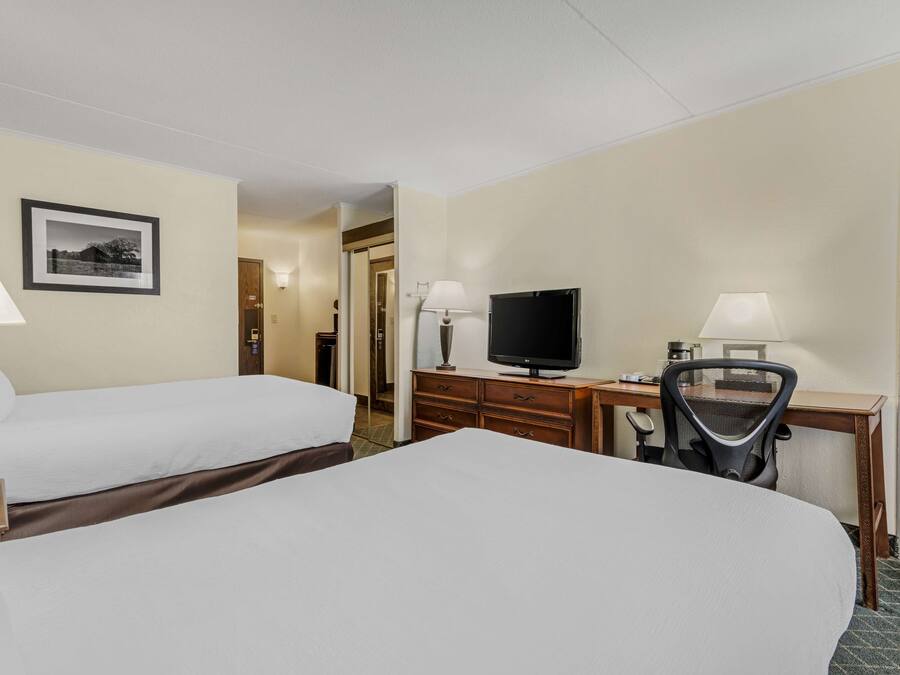 Una habitación de hotel con dos camas, un escritorio con televisor y una silla.
