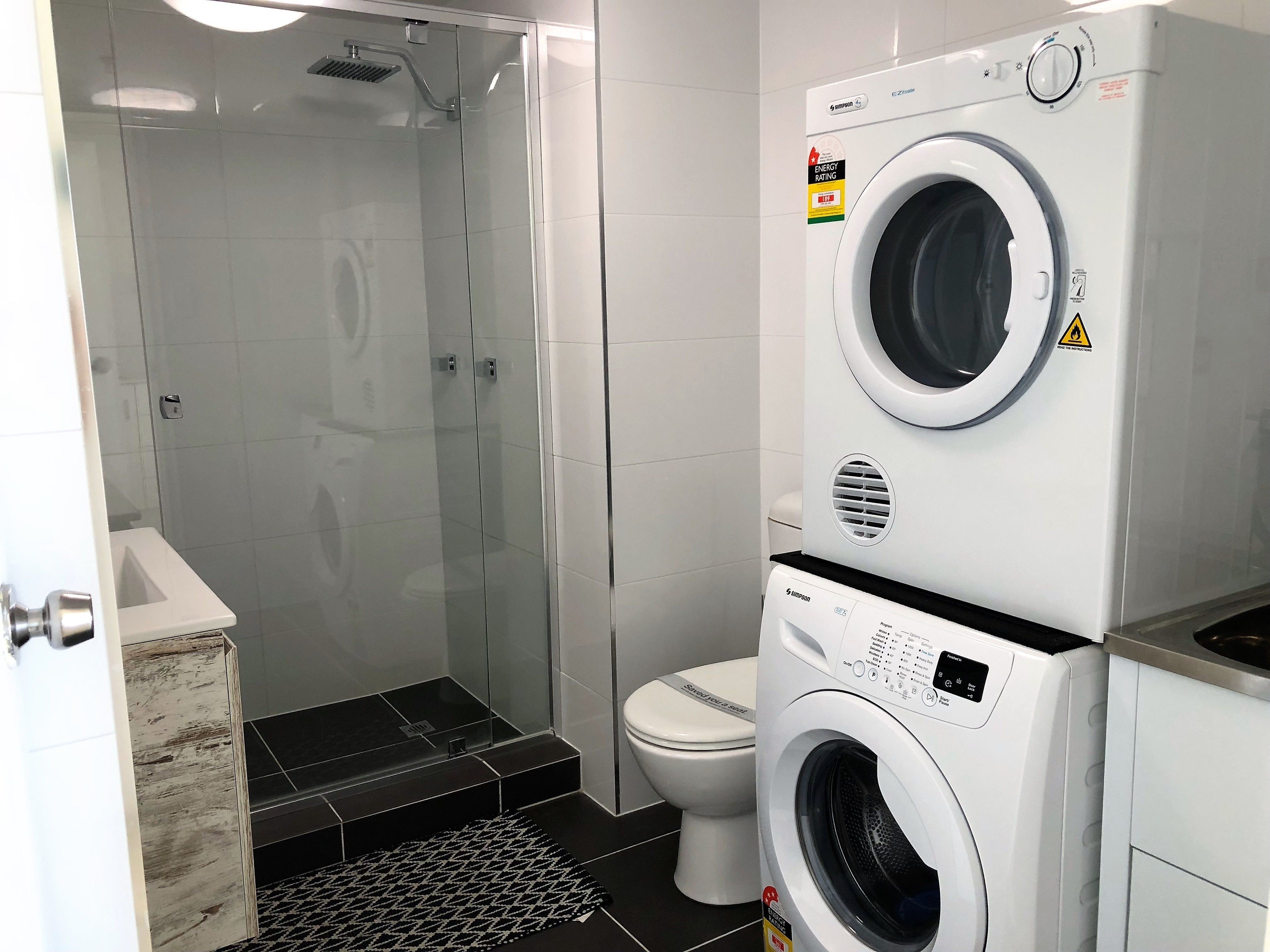 Een moderne badkamer met een douchecabine, een toilet en een gestapeld was- en droogprogramma.