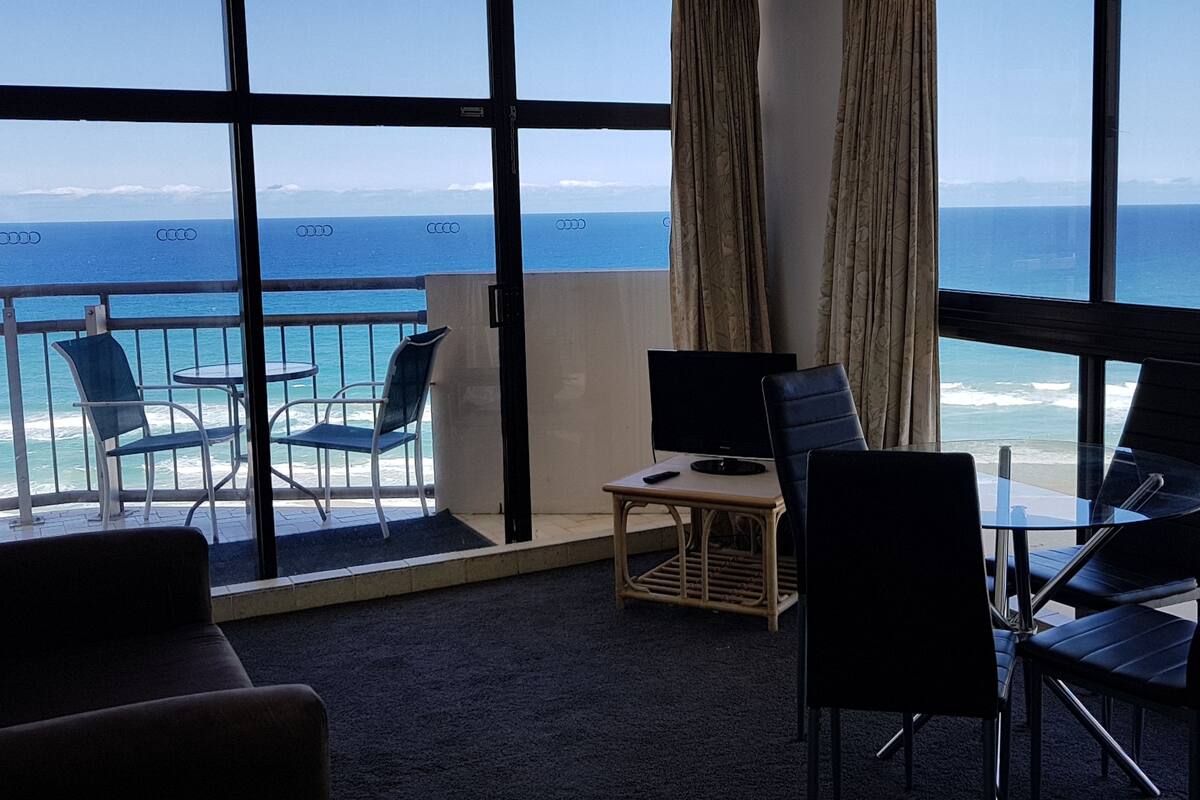A room with a large window overlooking the ocean, furnished with a sofa, chairs, and a small table.