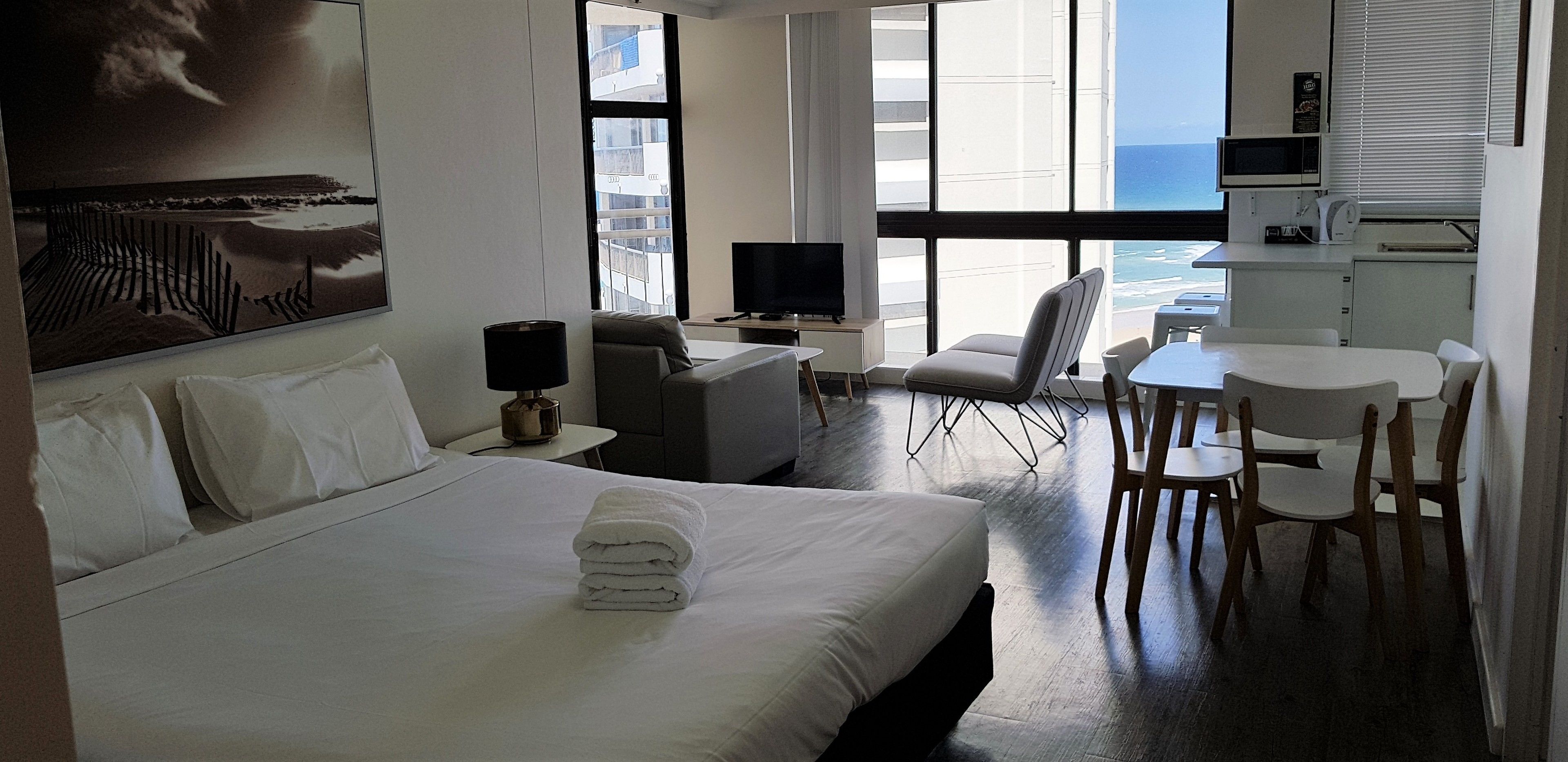 A hotel room with a bed, a desk, a chair, a television, and a view of the ocean.