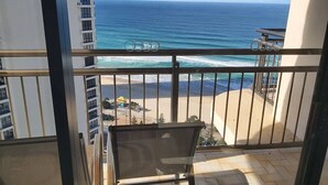 Un balcon avec vue sur l’océan et la plage, une rambarde en métal et une chaise.