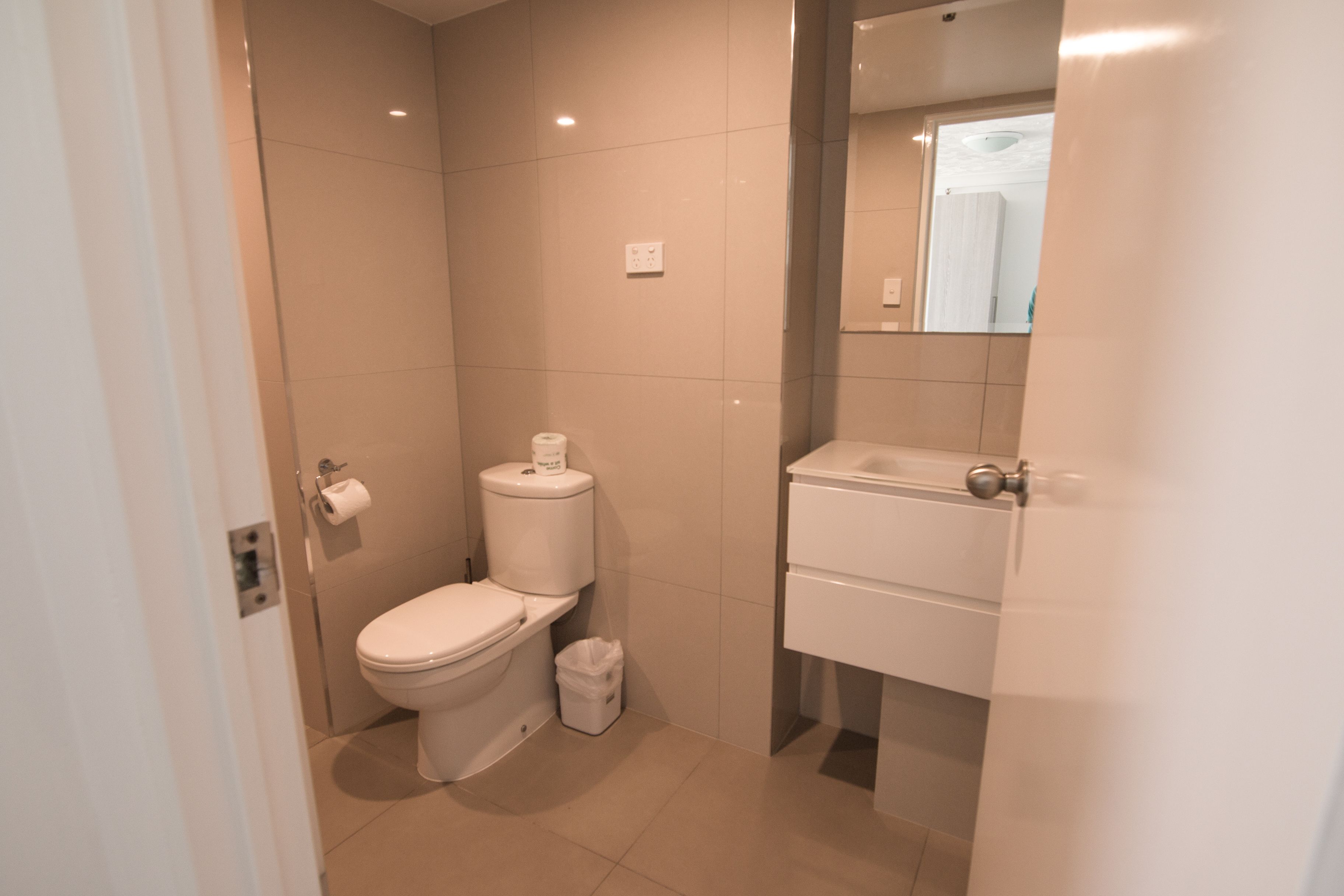 Een moderne badkamer met toilet, prullenbak en wastafel met spiegel erboven.