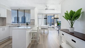 Une cuisine moderne avec des meubles blancs, un îlot central et un coin repas offrant une vue sur la ville.