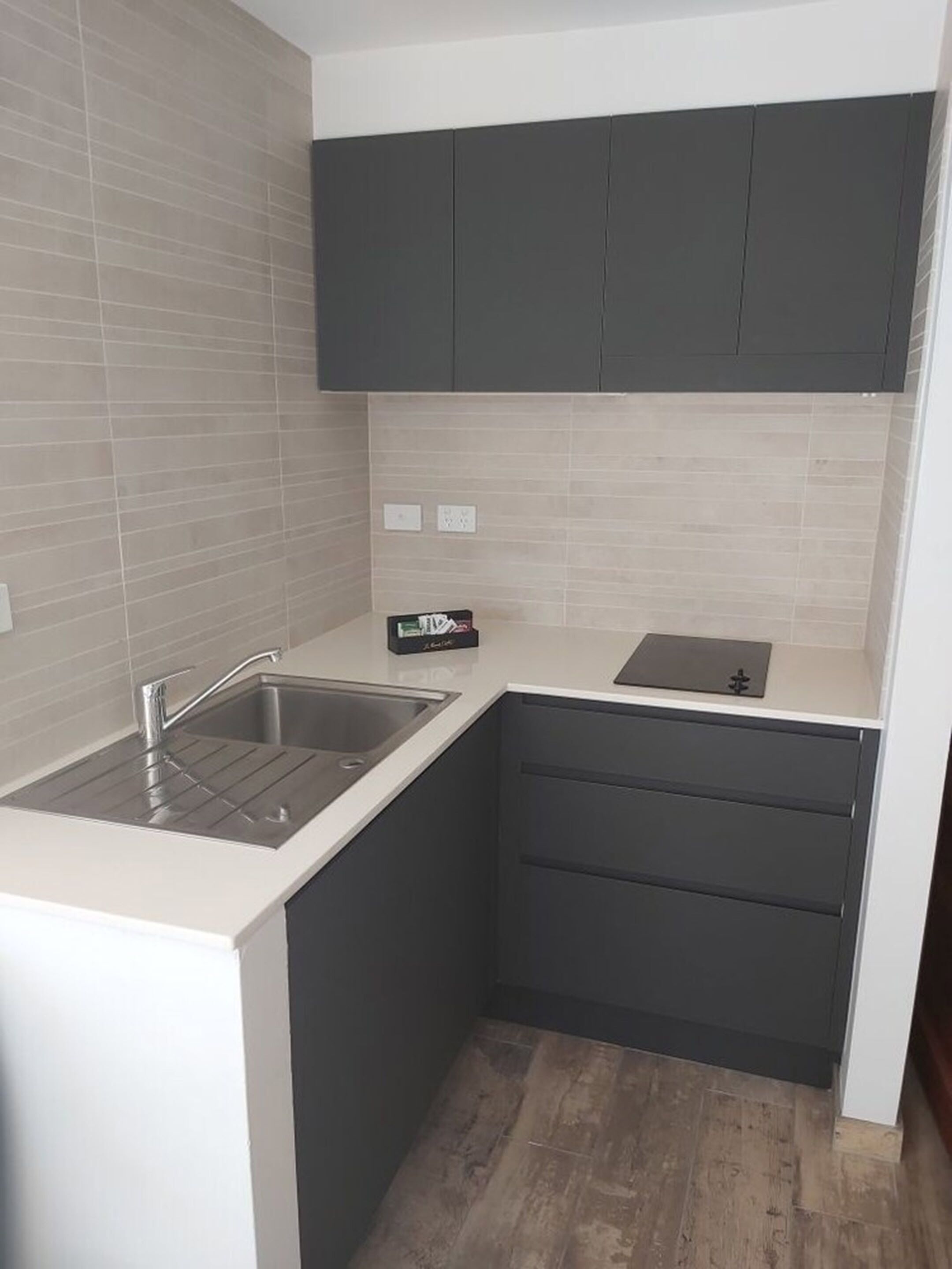 Een kleine keuken met een spoelbak, aanrecht en donkere kastjes.