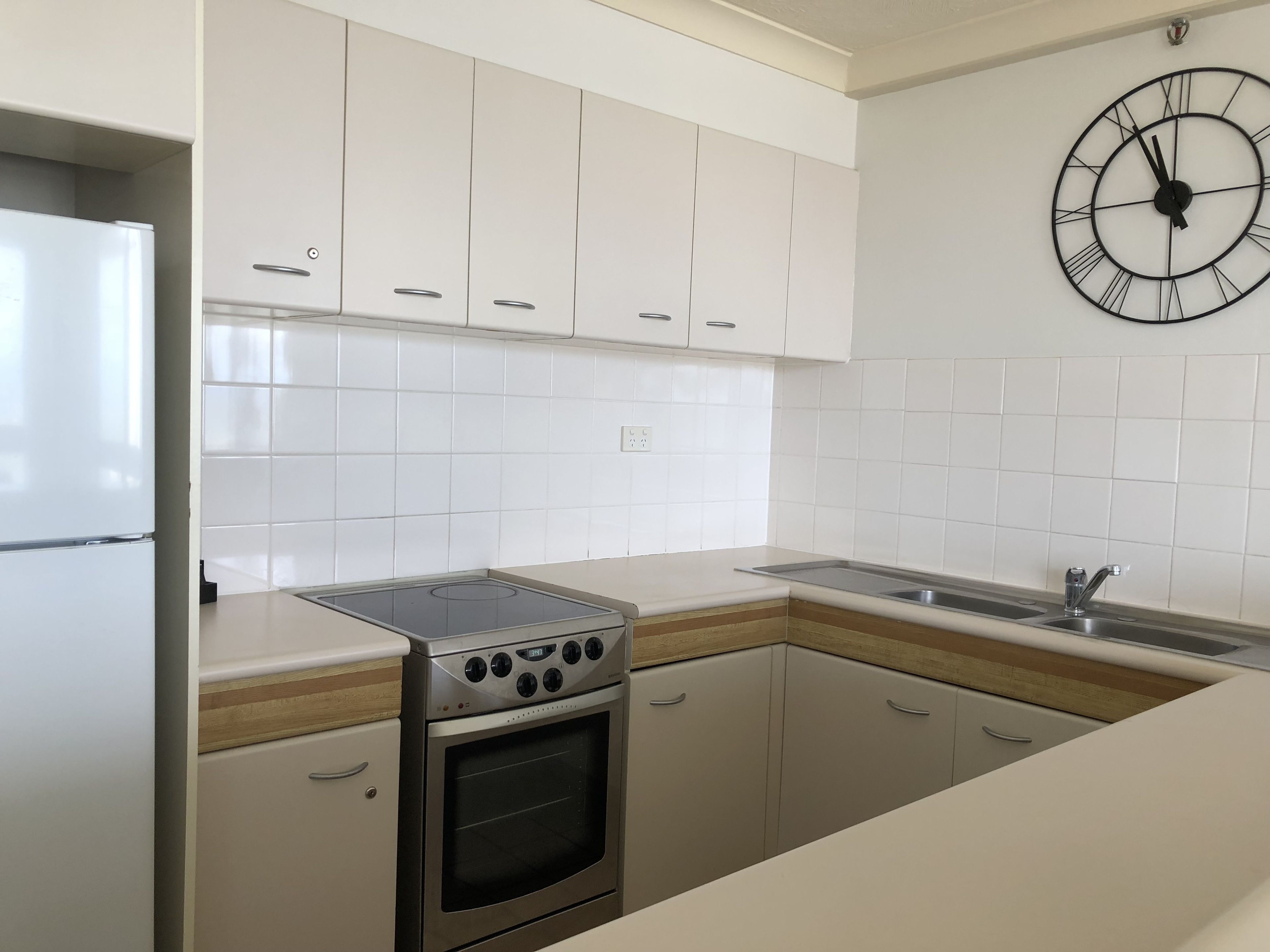 A modern kitchen with white cabinets, a stainless steel stove, a sink, and a wall clock.