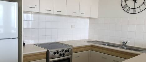 A modern kitchen with white cabinets, a stainless steel stove, a sink, and a wall clock.