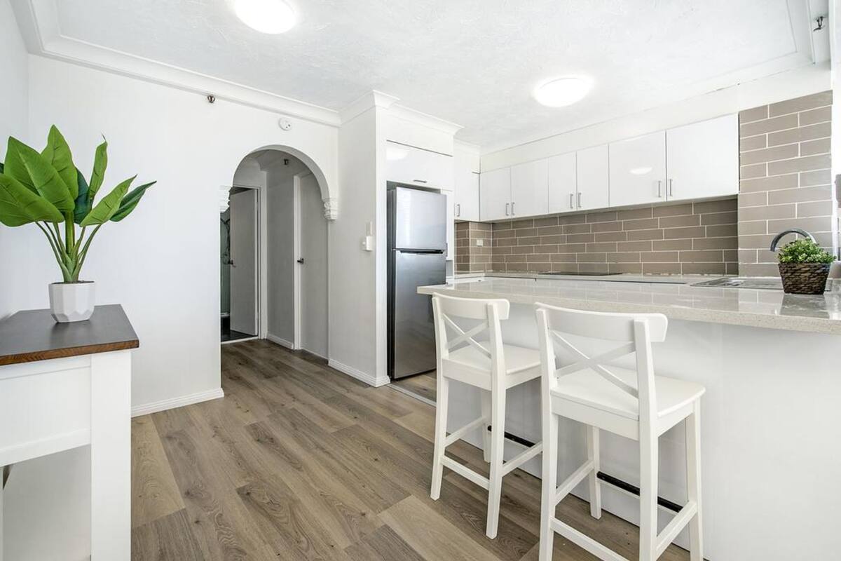 A modern kitchen with white cabinetry, a stainless steel refrigerator, and a wooden floor.