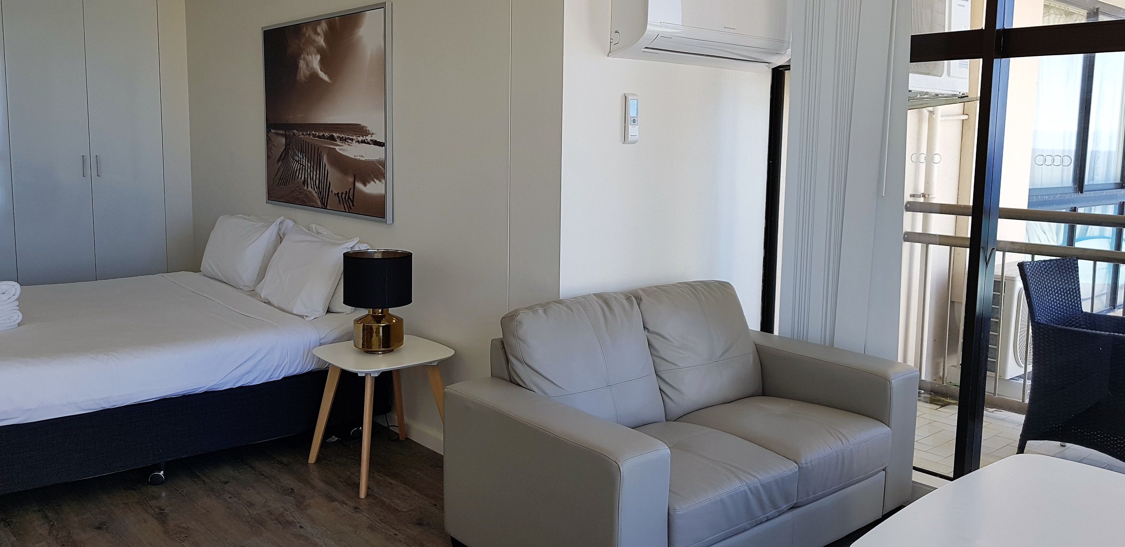 A hotel room with a bed, a small table with a lamp, a sofa, and a large window with a view.