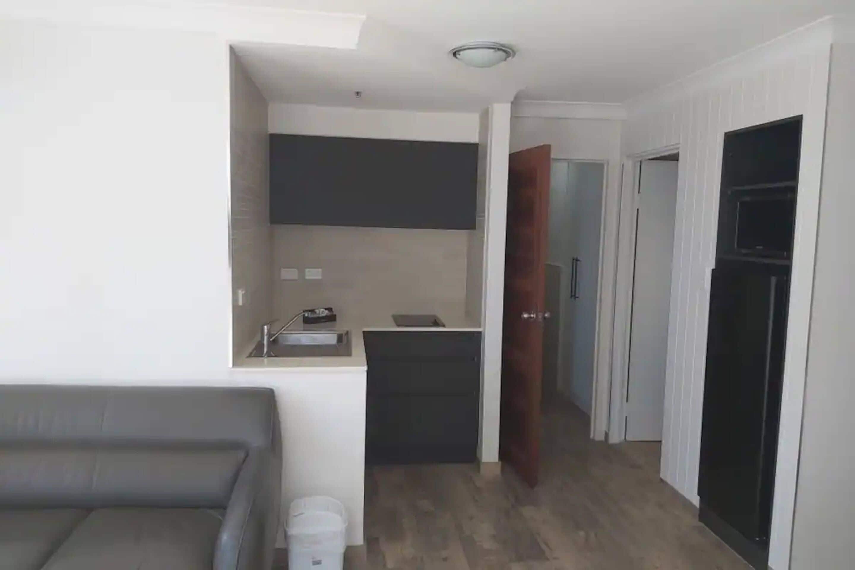 Un espacio habitable compacto con kitchenette, un sofá y una puerta que da a otra habitación.