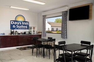 Una habitación de hotel con kitchenette, un comedor con mesa y sillas, un televisor de pantalla plana montado en la pared y una ventana con cortinas.
