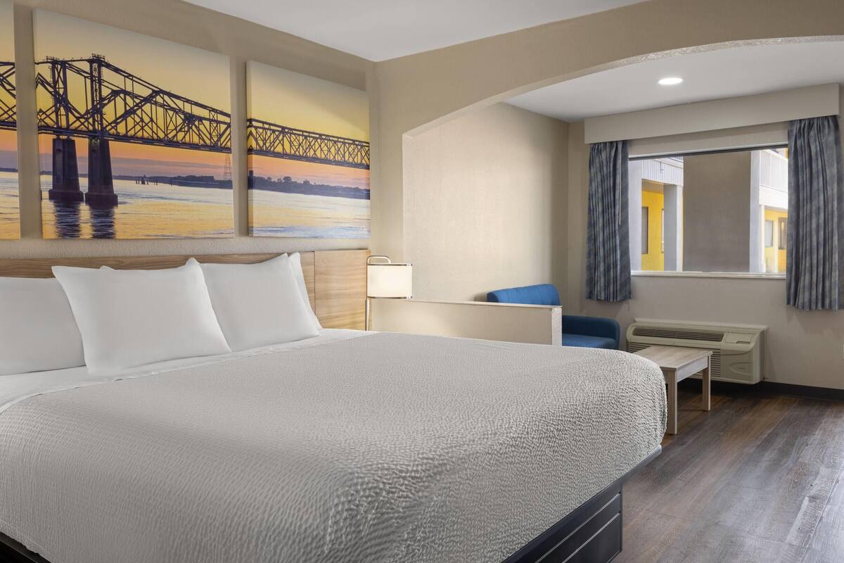 Habitación de hotel con una cama grande, un escritorio, una silla y un ventanal con cortinas.