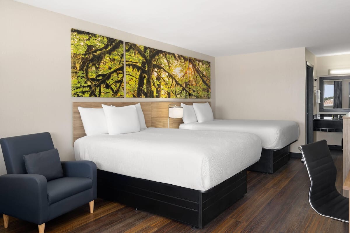 Habitación de hotel con una cama grande, dos mesitas de noche, una silla y un cuadro en la pared.