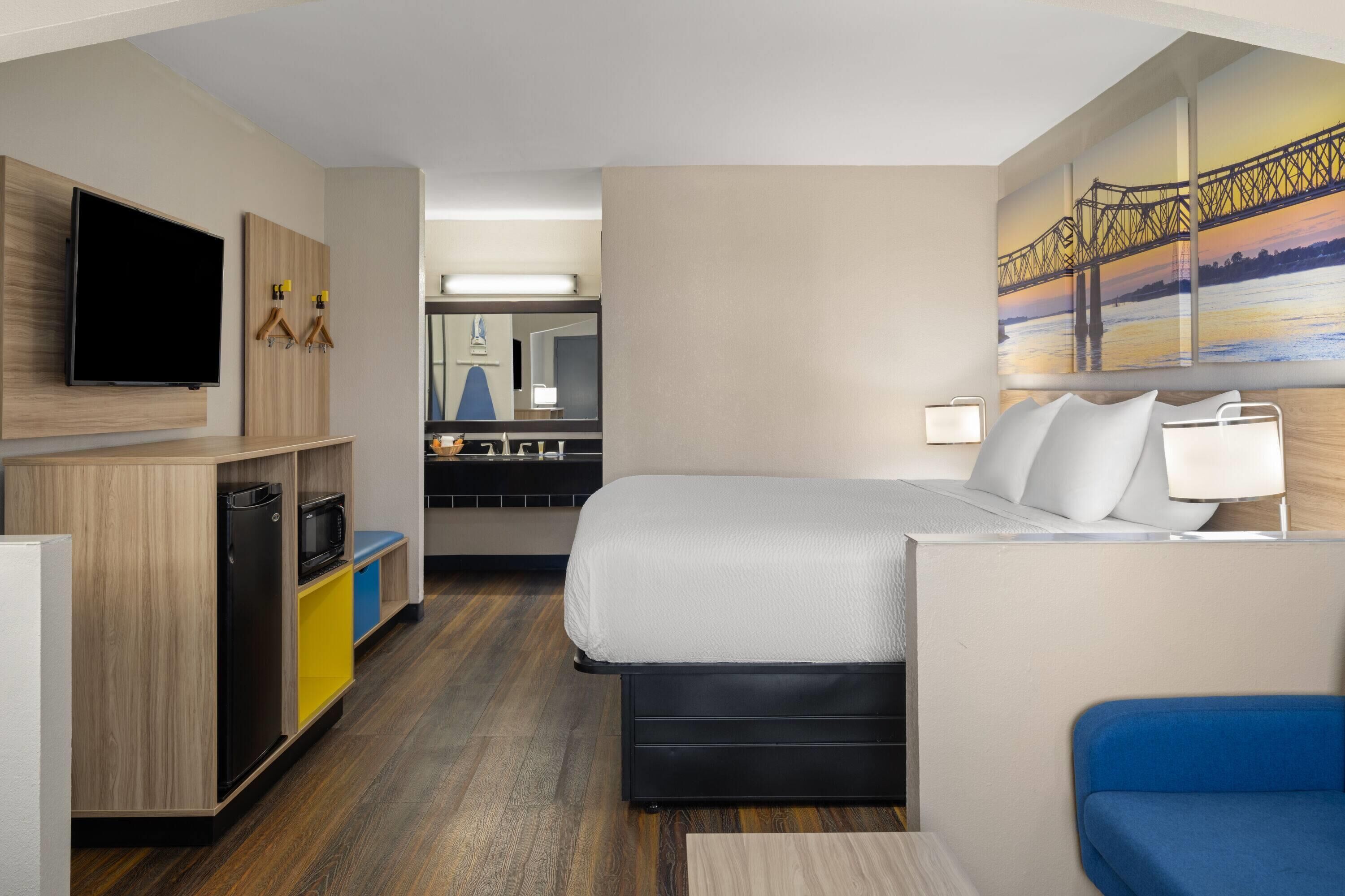 Una habitación de hotel con cama, televisor, escritorio y kitchenette.