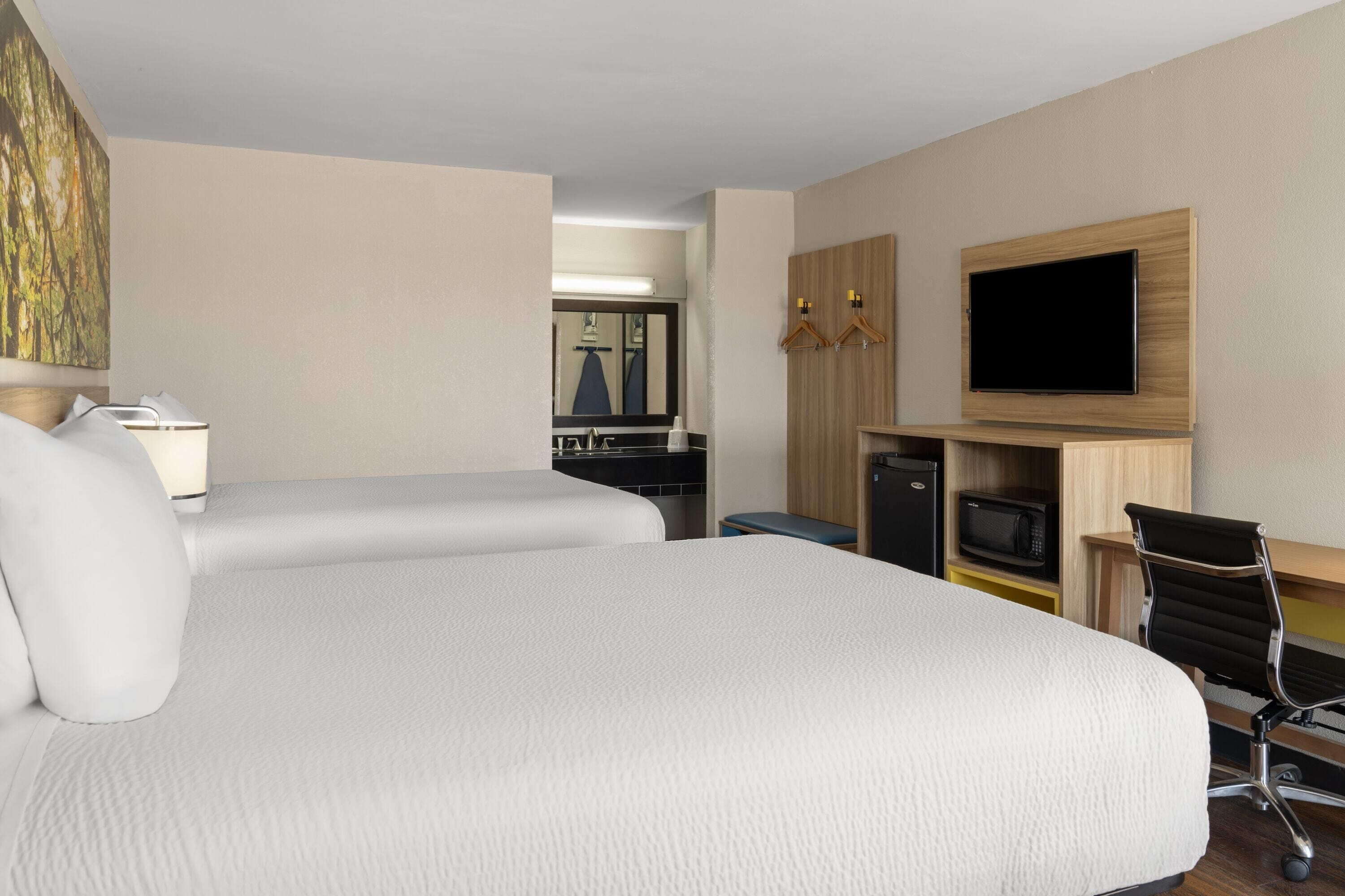 A hotel room with a large bed, a desk with a flat-screen TV, a microwave, and a seating area with a chair.