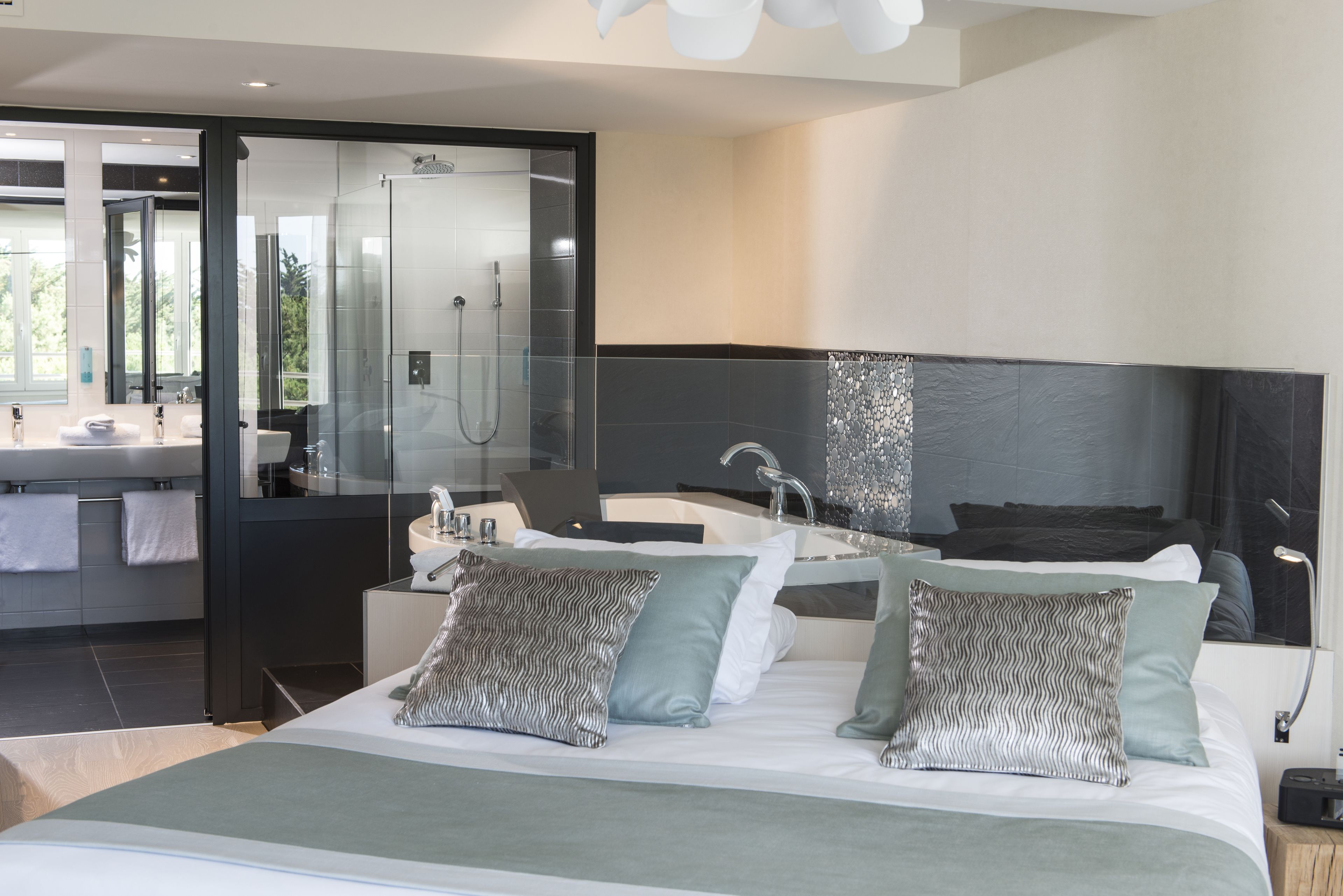 A modern hotel room with a large bed, a separate bathroom with a glass shower, and a view of the outdoors.