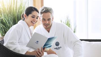 Dos personas con batas blancas sentadas en una silla de mimbre, leyendo un folleto con una imagen de playa.