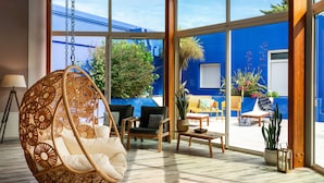 A spacious room with a hanging chair, wooden furniture, and large windows offering a view of the outside. - Hôtel Valdys Thalasso & Spa - les Pins (Saint-Jean-de-Monts)