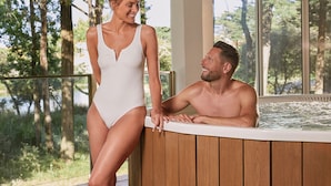 A couple in a hot tub with a wooden deck and a view of trees. - Hôtel Valdys Thalasso & Spa - les Pins (Saint-Jean-de-Monts)