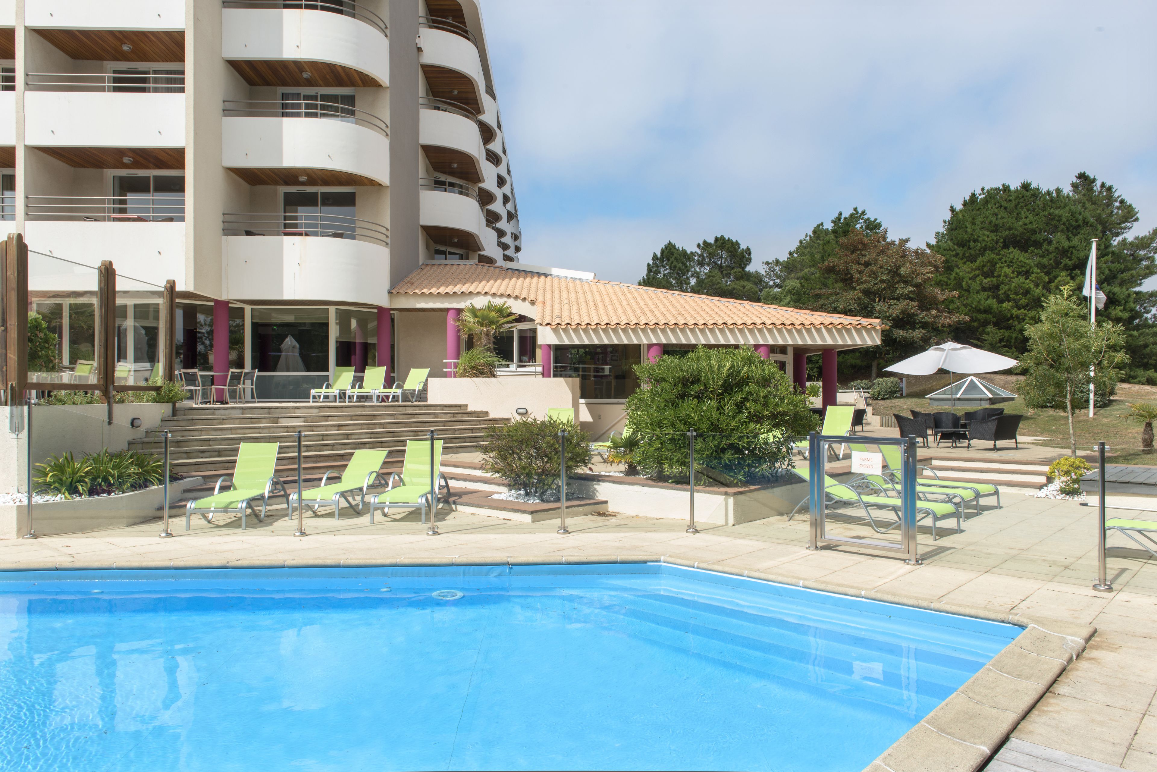 A swimming pool with lounge chairs, a covered patio, and a multi-story building with balconies.