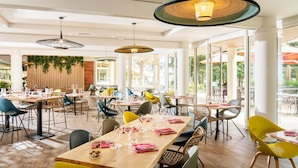 A spacious indoor dining area with multiple tables and chairs, large windows, and hanging pendant lights. - Hôtel Valdys Thalasso & Spa - les Pins (Saint-Jean-de-Monts)