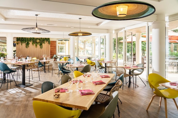 Un amplio comedor interior con varias mesas y sillas, ventanas grandes y lámparas colgantes.
