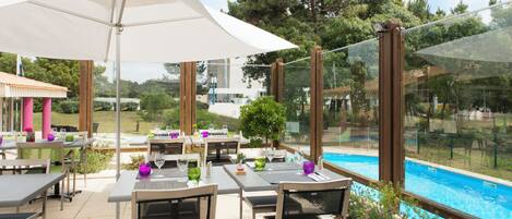 Un espacio exterior para comer con mesas, sillas, sombrillas y vistas a una piscina.