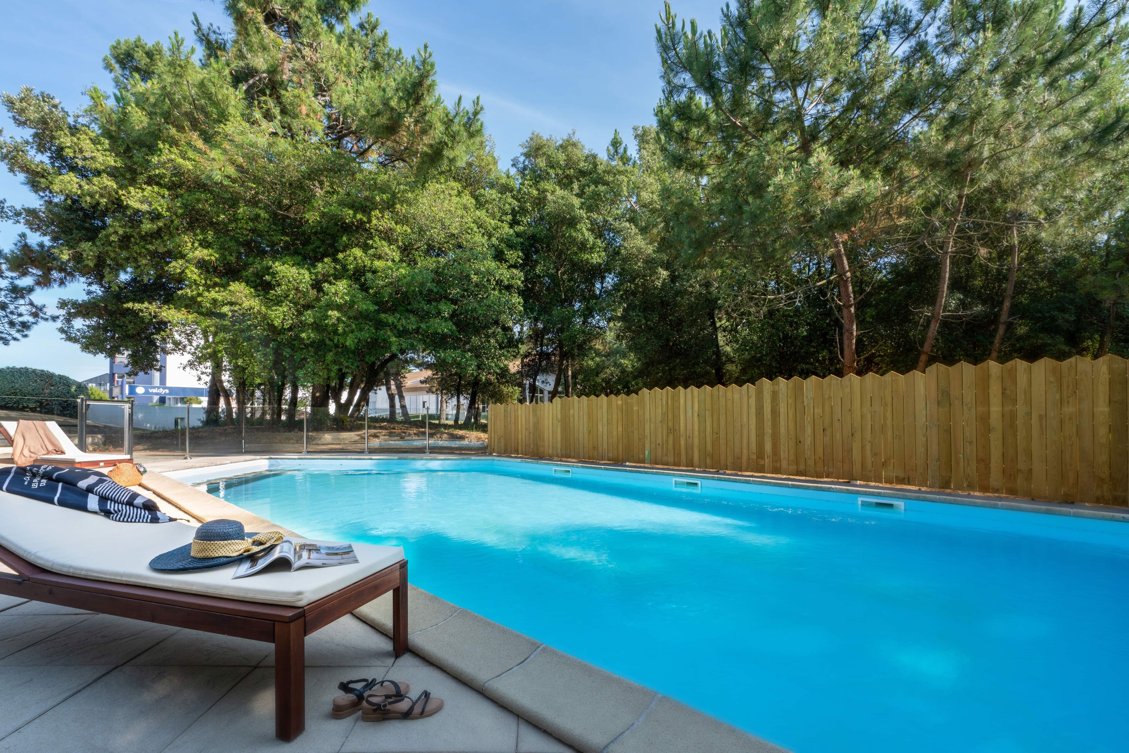 A swimming pool with a wooden fence, lounge chairs, and a tiled deck.