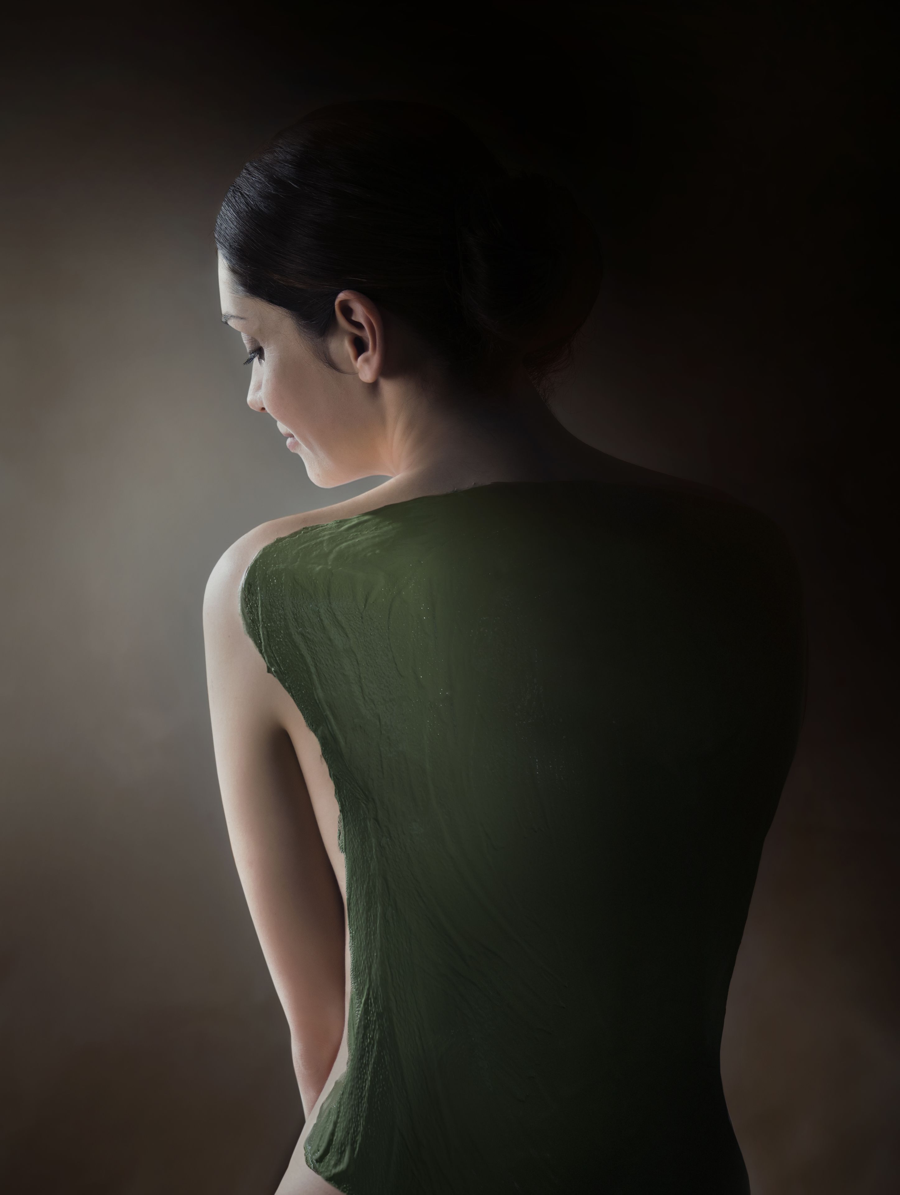 A person in a green dress standing against a dark background.