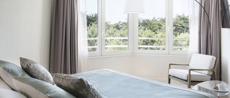 Quarto de hotel moderno com uma cama grande, uma cadeira, uma mesinha e uma televisão.
