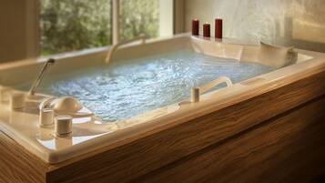 A wooden bathtub with a glass enclosure, a handheld showerhead, and candles on the edge.