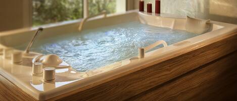 A wooden bathtub with a glass enclosure, a handheld showerhead, and candles on the edge.