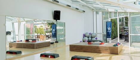 A spacious room with large windows, a mirrored wall, and exercise equipment.