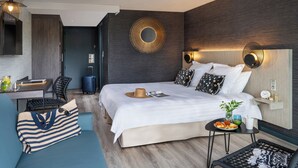 A modern hotel room with a large bed, a desk, a sofa, and a small table with breakfast. - Hôtel Valdys Thalasso & Spa - les Pins (Saint-Jean-de-Monts)