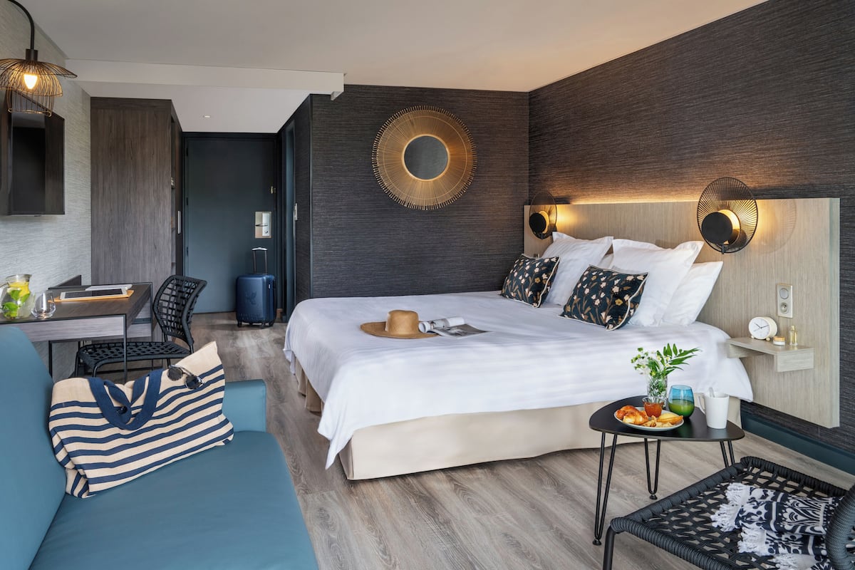 Ein modernes Hotelzimmer mit einem großen Bett, einem Schreibtisch, einer Couch und einem kleinen Tisch mit Frühstück.