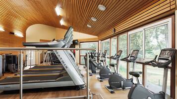 Un gimnasio con cintas de correr, elípticas y bicicletas estáticas, que cuenta con techos de madera y ventanas amplias.