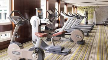 Varias bicicletas estáticas en un gimnasio de hotel, con alfombra a rayas y ventanas amplias.