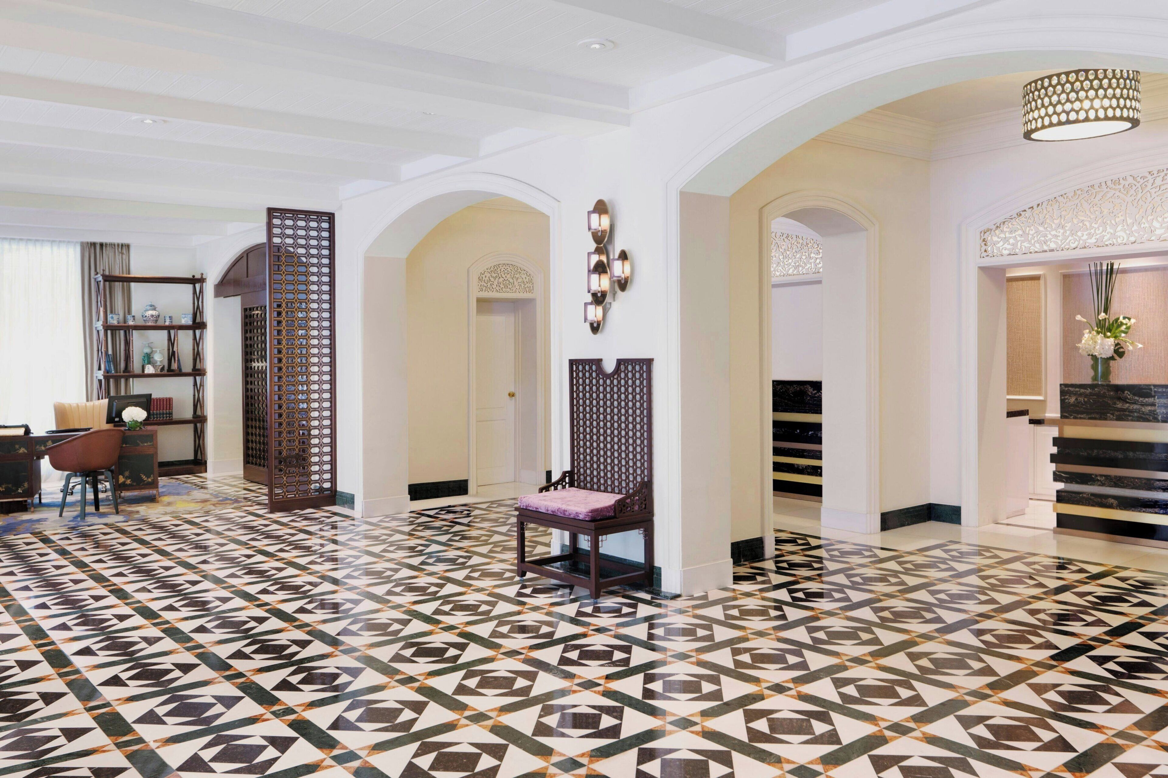 Een hotelhal met een vloer met een geometrisch patroon, een receptiebalie, een zithoek en een trap.