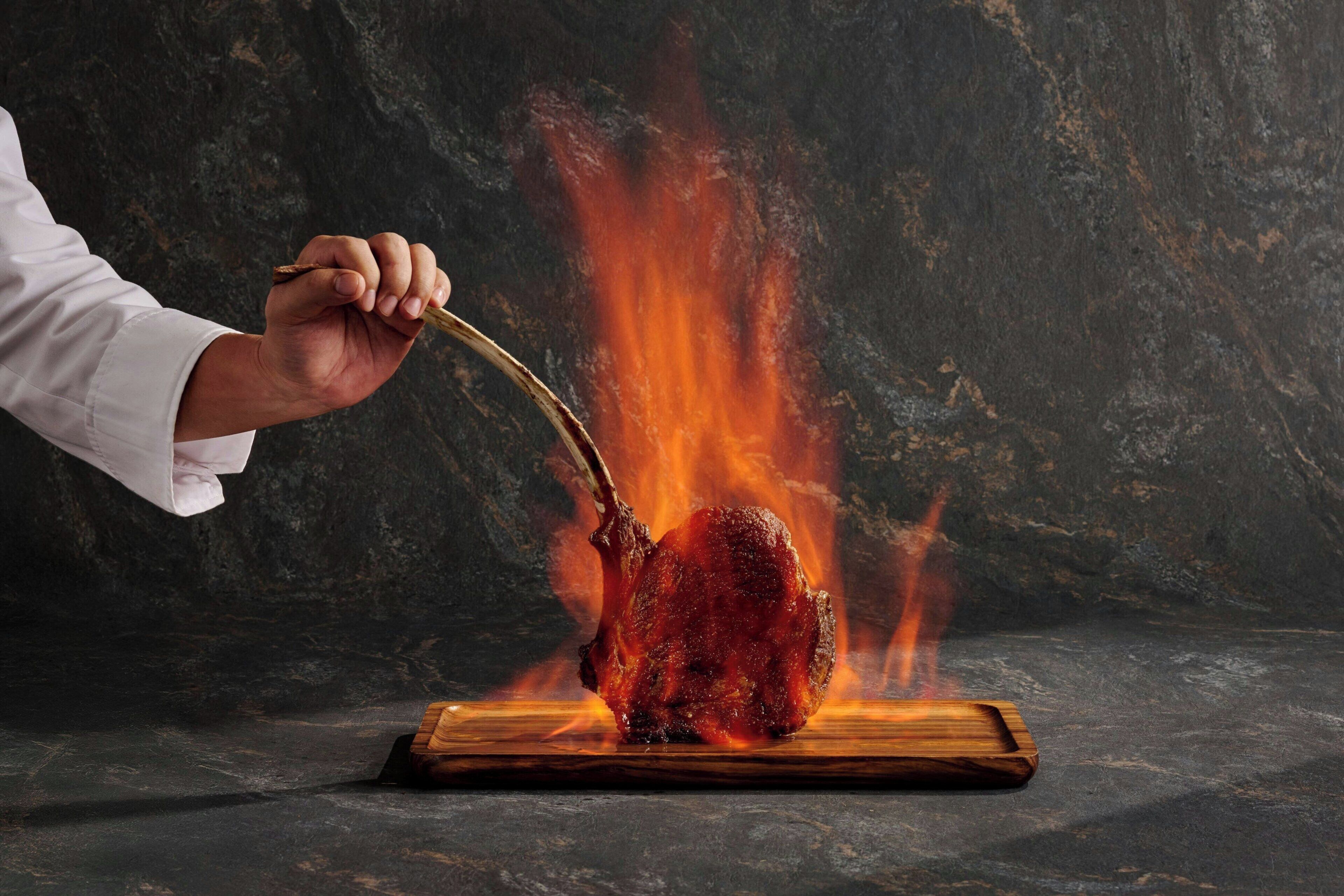 A hand holding a fork over a flaming object on a wooden board.