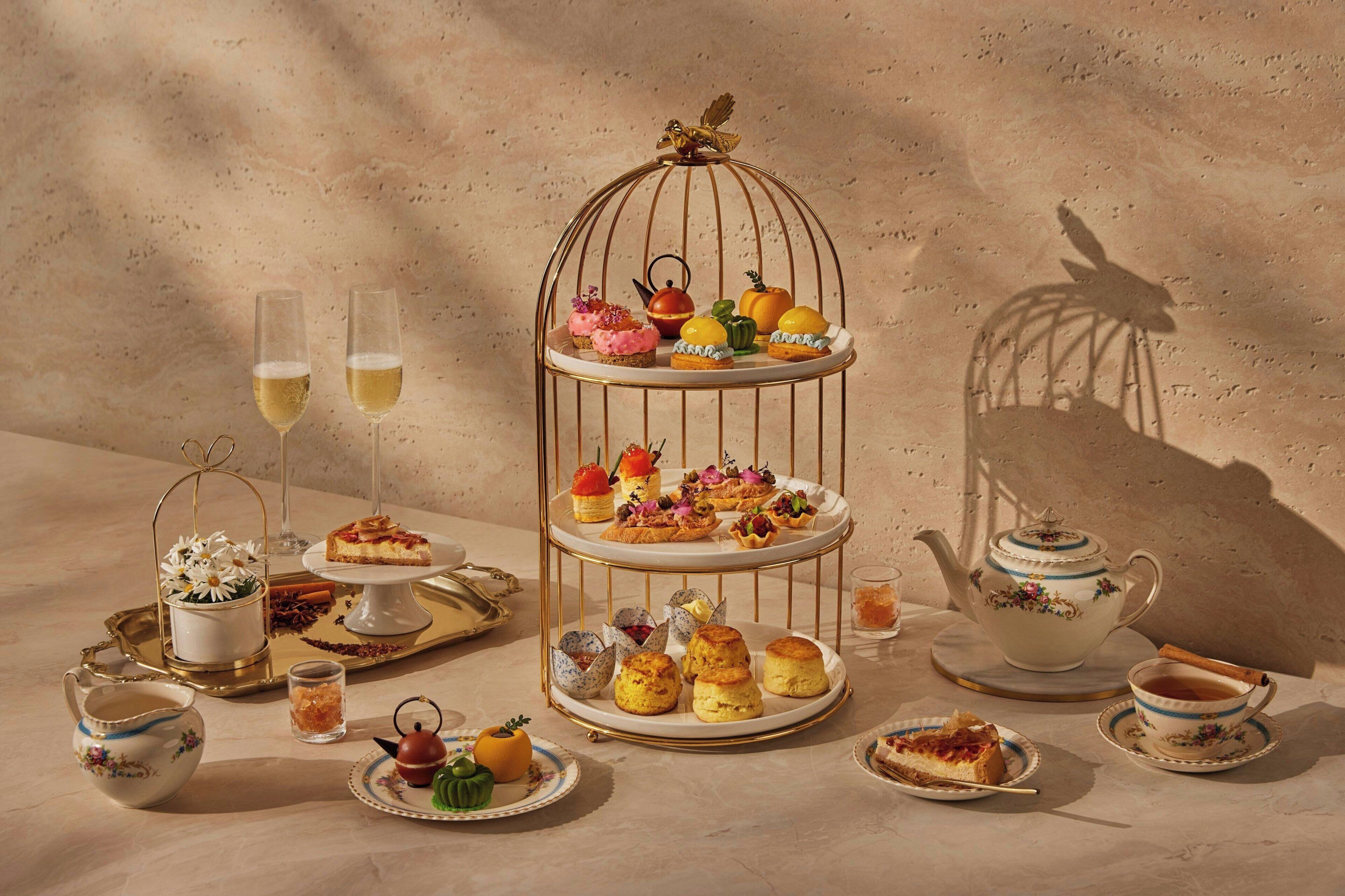 A tiered dessert stand with various pastries and a teapot on a table.