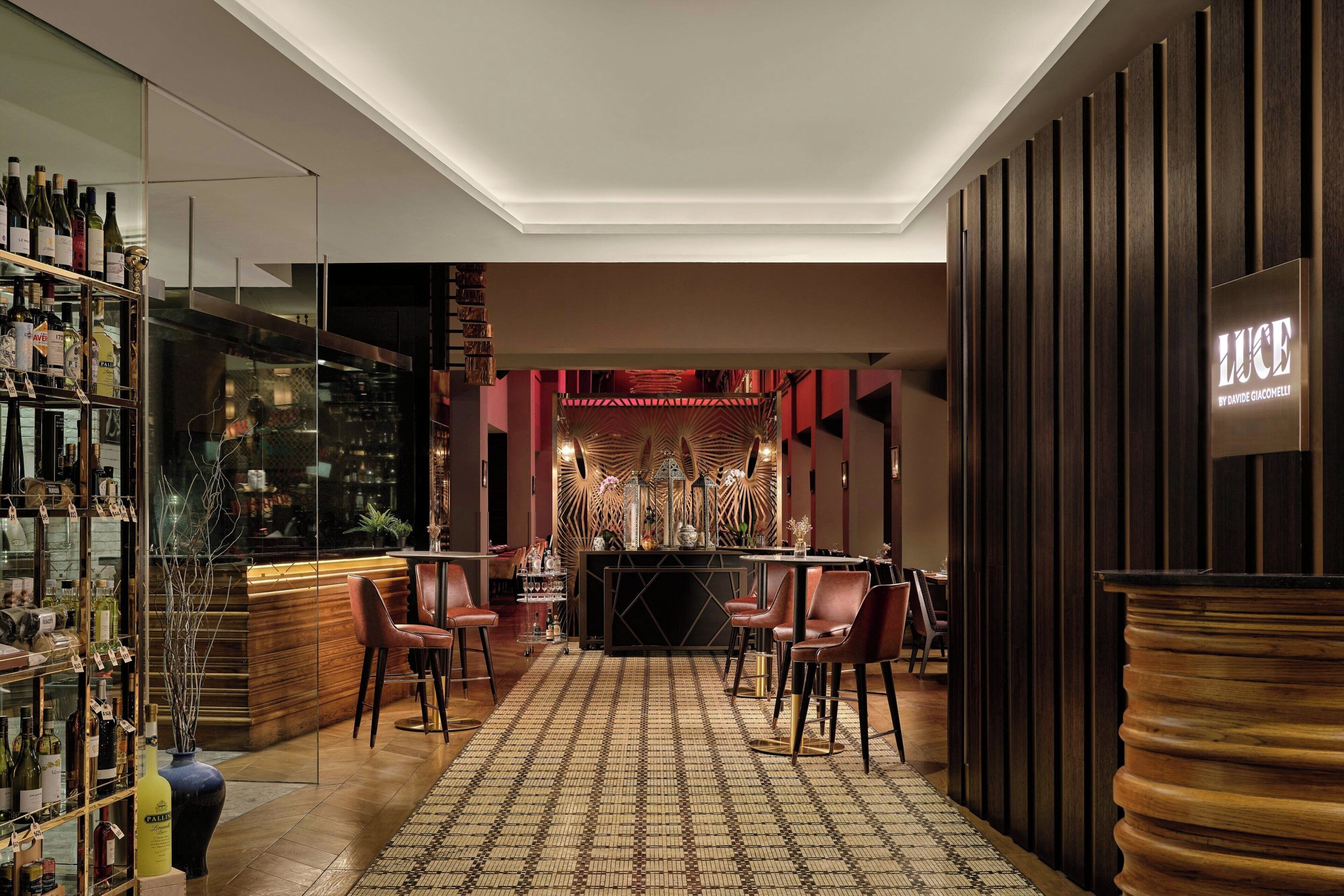 A bar area with a wooden bar counter, multiple chairs, and a patterned floor.