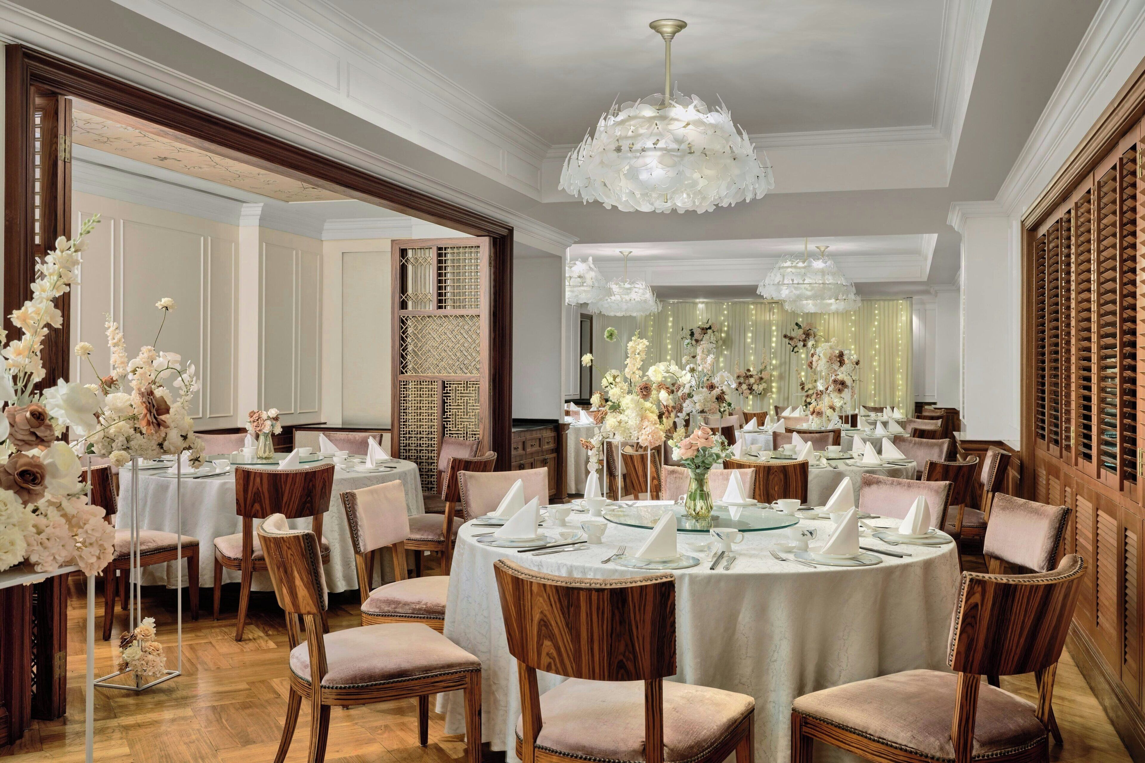 A formal dining room with round tables, wooden chairs, and floral centerpieces.