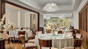 A formal dining room with round tables, wooden chairs, and floral centerpieces.