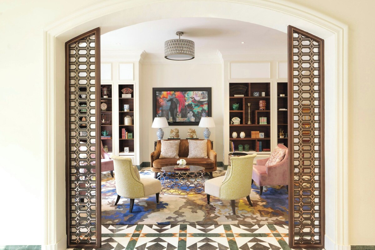Un salon comprenant un canapé, deux fauteuils, une table basse, un tapis à motifs et une bibliothèque.